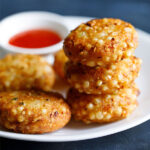 closeup shot of a stack of sabudana vada on top of each other in a white plate with red chilli sauce in a white bowl