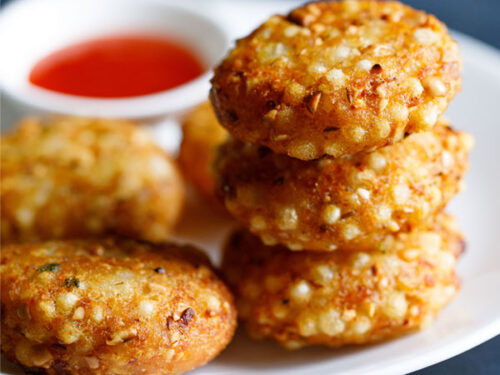 closeup shot of a stack of sabudana vada on top of each other in a white plate with red chilli sauce in a white bowl