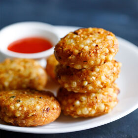 Close-up of a pile of Sabudana vada in a white plate with red chilli paste and red chilli paste in a white bowl