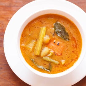sambar filled in a white bowl placed on white plate on a brown wooden board