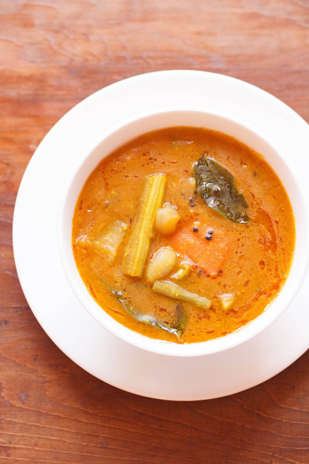 sambar filled in a white bowl placed on white plate on a brown wooden board
