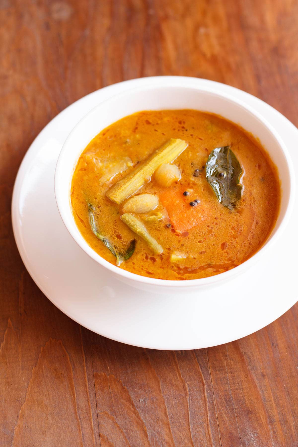 sambar filled in a white bowl placed on white plate on a brown wooden board