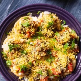 overhead shot of sev puri on a dark purple plate on a a dark blue table