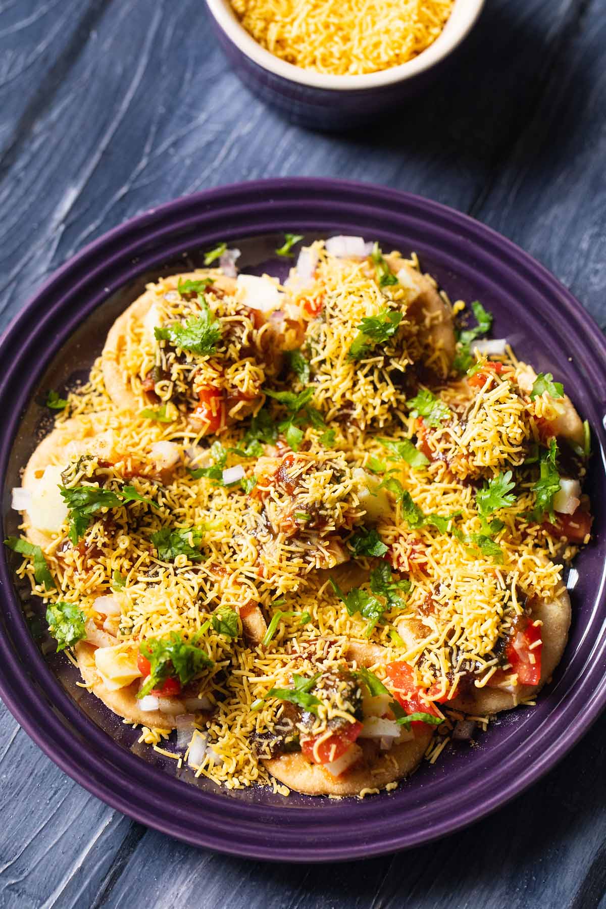 overhead shot of sev puri on a dark purple plate on a a dark blue table