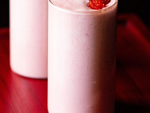 strawberry milkshake topped with strawberry slices in 2 glasses on a reddish pink tray.
