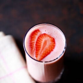 strawberry smoothie in a glass topped with strawberry slices with a cream napkin on a dark black-brown board