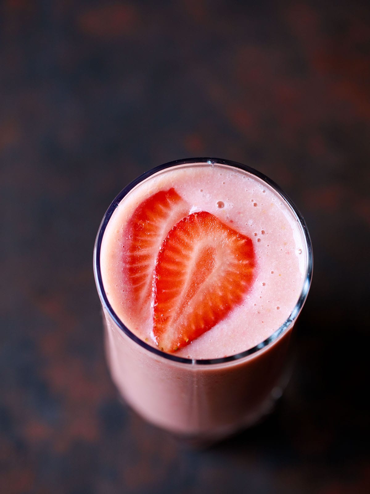 strawberry banana smoothie in a glass topped with strawberry slices on a dark black-brown board