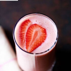 strawberry smoothie in a glass topped with strawberry slices with a cream napkin on a dark black-brown board