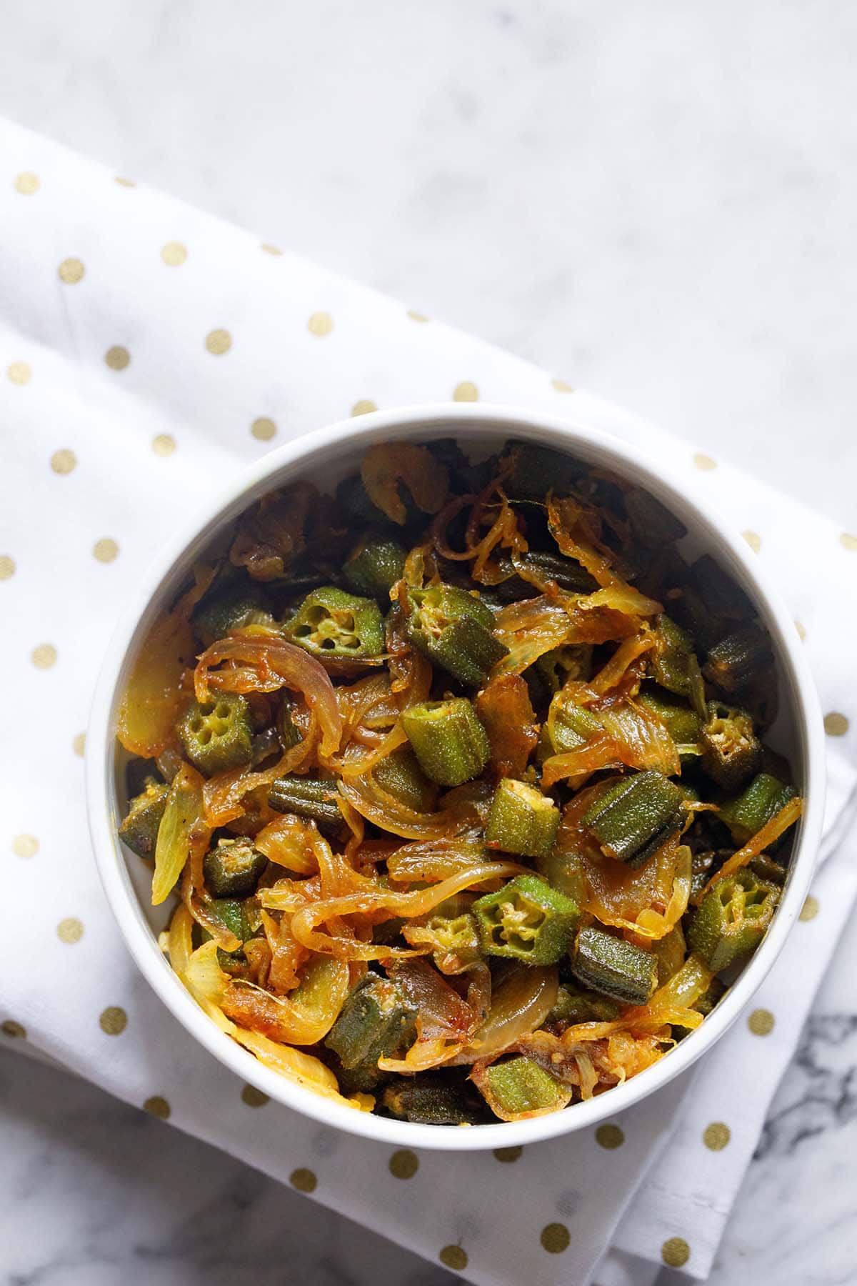 bhindi do pyaza in a white bowl on a golden polka dotted white napkin