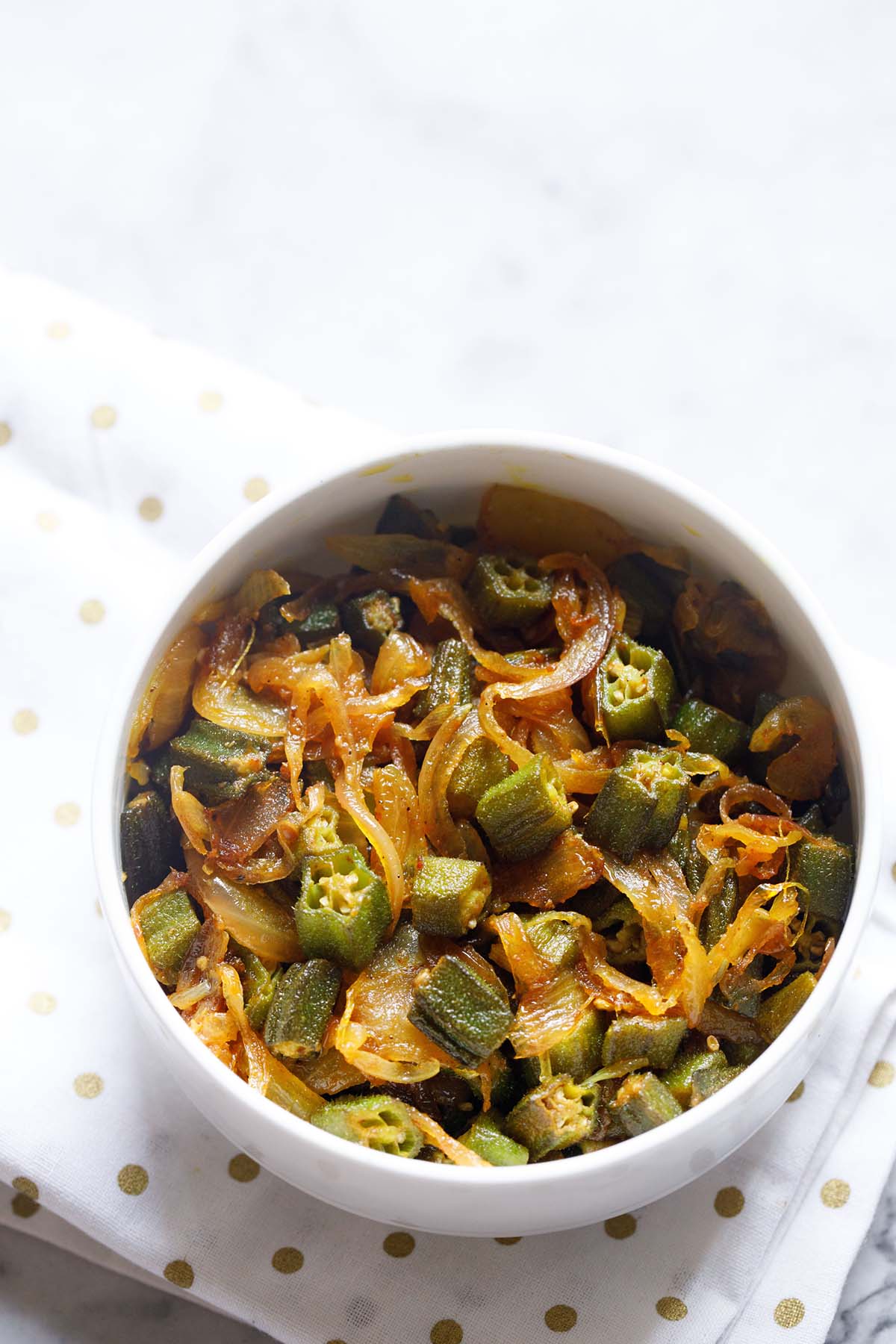 bhindi do pyaza in a white bowl on a golden polka dotted white napkin