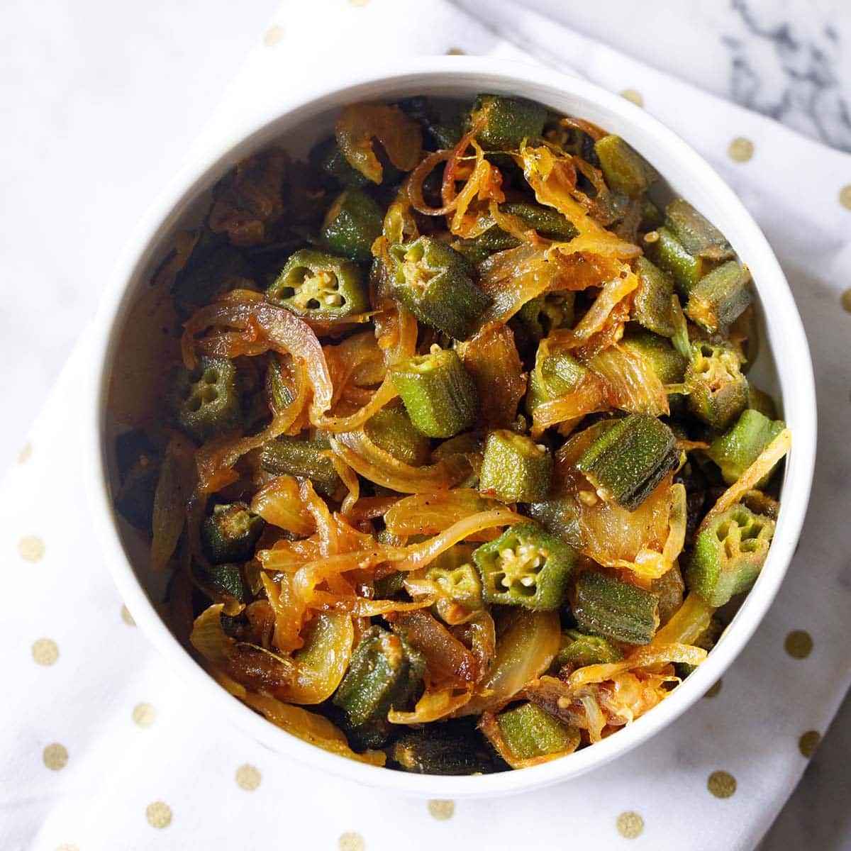 bhindi do pyaza in a white bowl on a golden polka dotted white napkin