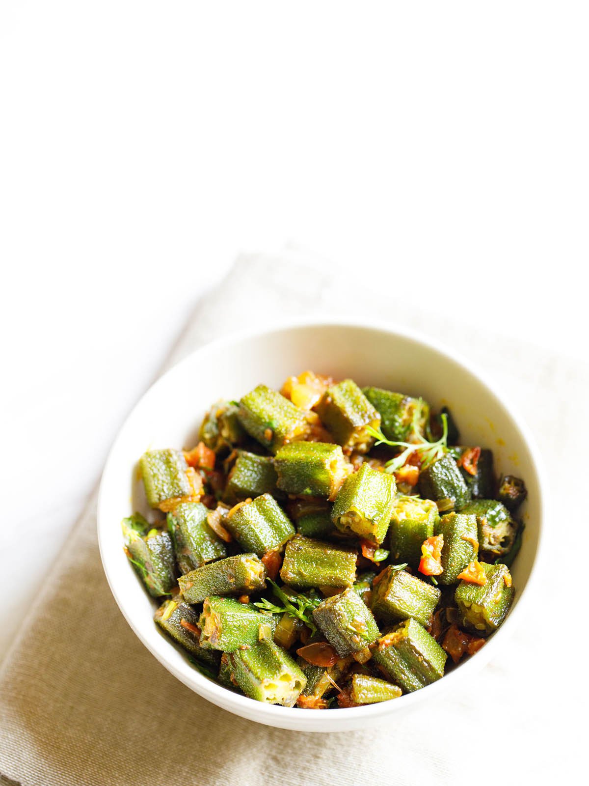 bhindi masala served in a white bowl on an off white napkin on a white background. 