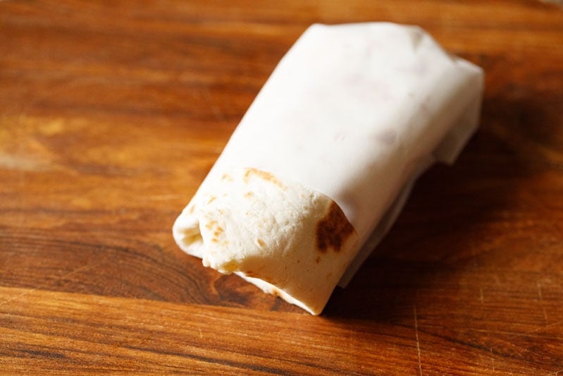 burrito wrapped in butter paper on a wooden board