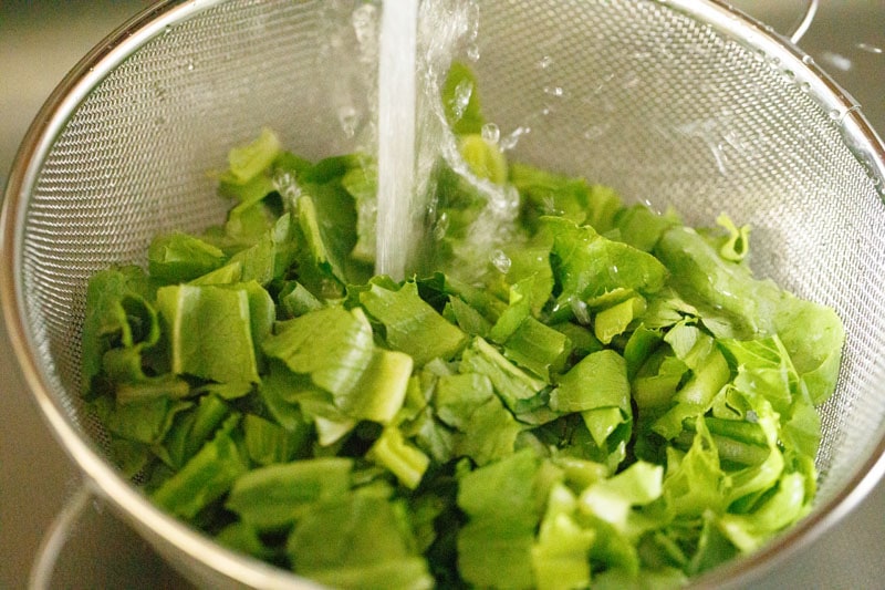 rinsing romaine lettuce pieces in a mesh colander