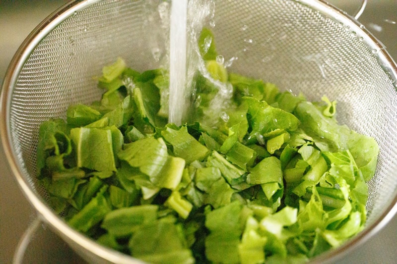 rinsing romaine lettuce pieces in a mesh colander