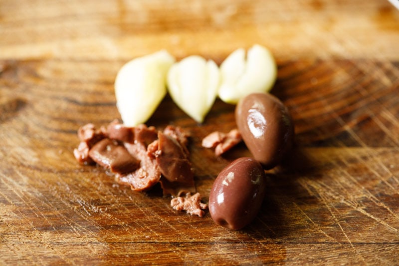 garlic cloves and pitted kalamata olives on a wooden cutting board