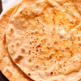 paneer paratha kept on top of another paratha on a white plate and topped with butter.