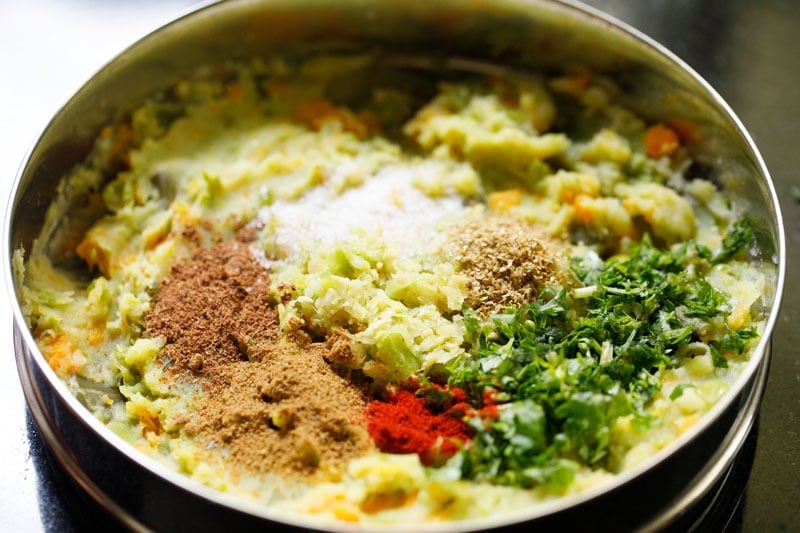 seasonings, ground spices and coriander leaves on top of the mashed vegetables