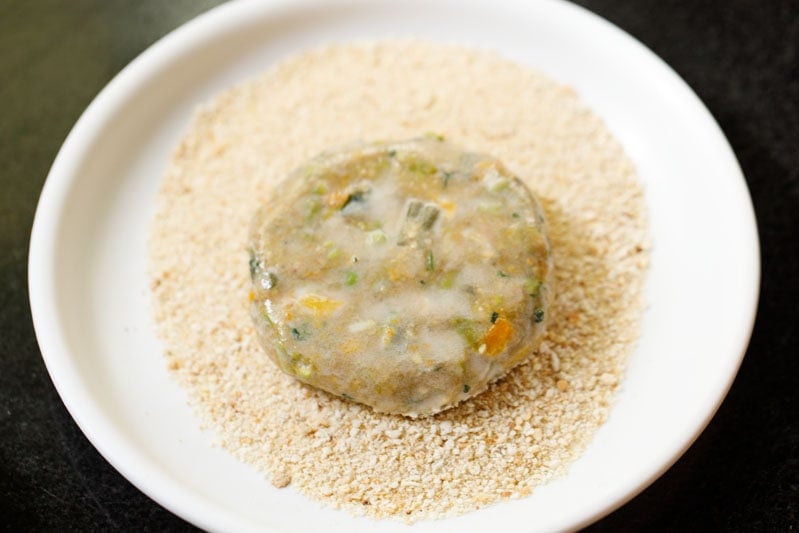 batter coated veg cutlet on breadcrumbs in a white plate