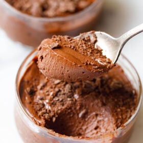 closeup shot of eggless chocolate mousse scooped in a silver spoon showing its light fluffy texture held above a bowl filled with the mousse