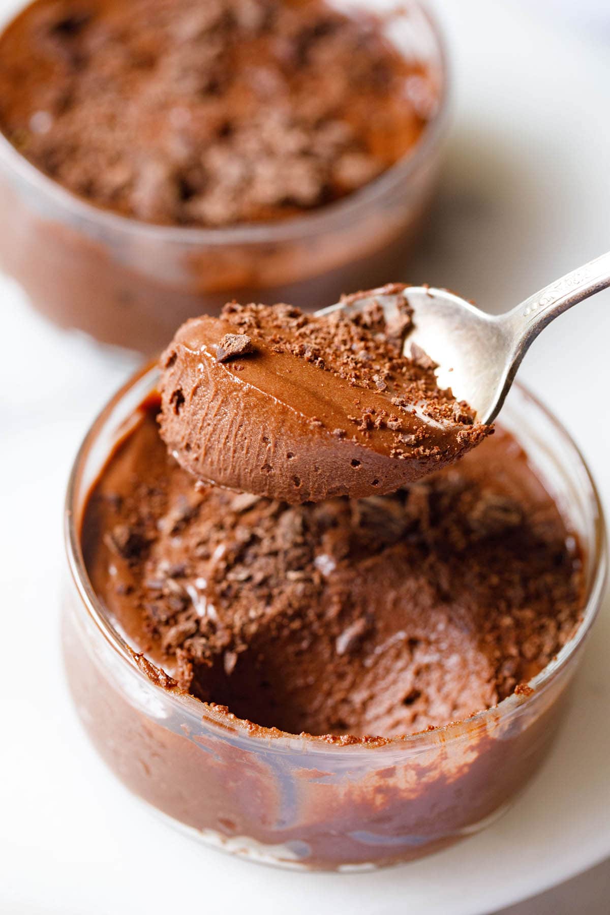 closeup shot of eggless chocolate mousse scooped in a silver spoon showing its light fluffy texture held above a bowl filled with the mousse