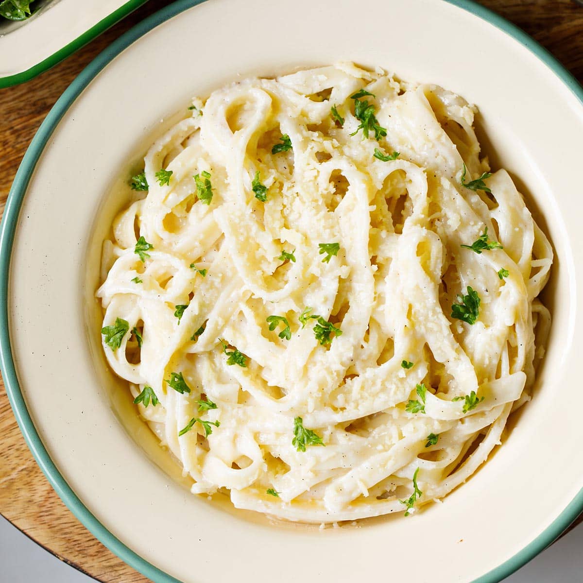 overhead shot of fettuccine alfredo sprinkled with grated parmesan and chopped parsley filled in a deep dish plate