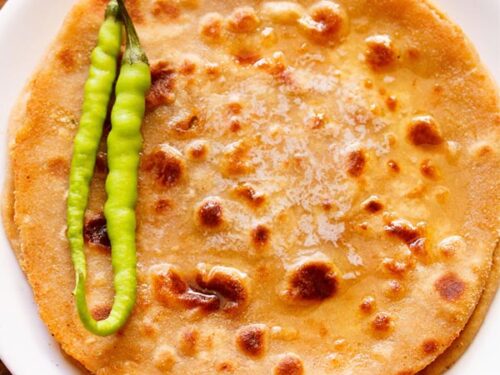 overhead shot of gobi paratha in a white plate topped with two green chillies at the side