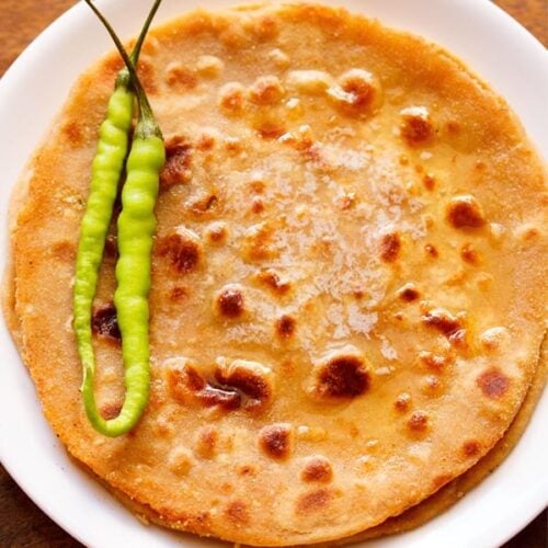 overhead shot of gobi paratha in a white plate topped with two green chillies at the side