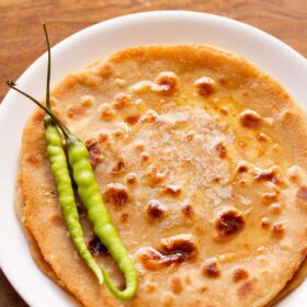 overhead shot of gobi paratha in a white plate topped with two green chillies at the side