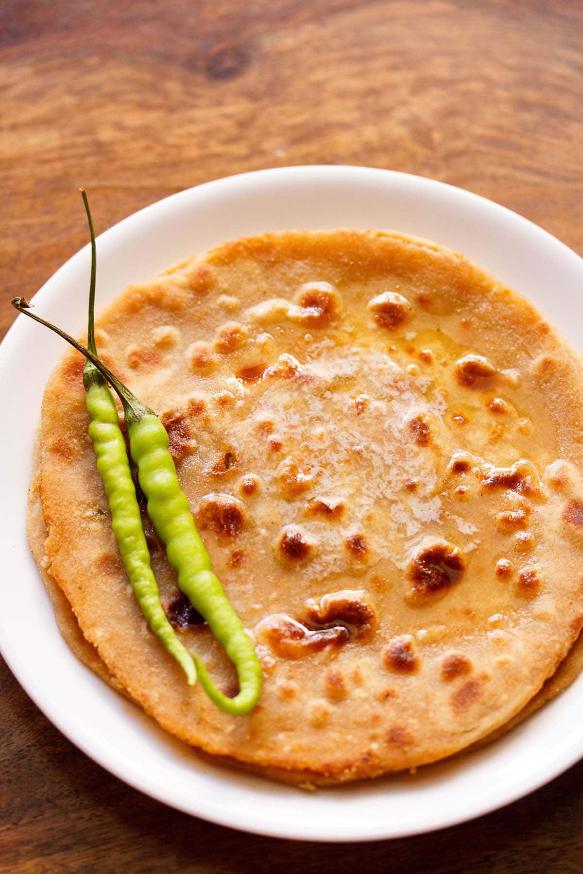 overhead shot of gobi paratha in a white plate topped with two green chillies at the side