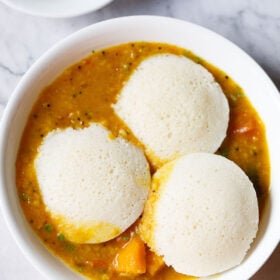 three idli on top of a layer of sambar in a white bowl