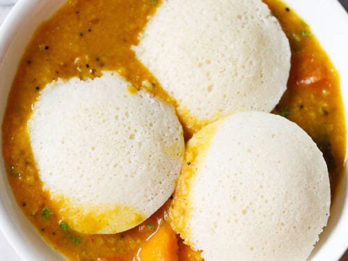 three idli on top of a layer of sambar in a white bowl