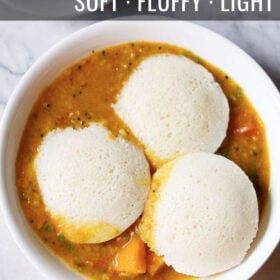 overhead shot of three idli on top of a layer of sambar in a white bowl with text layovers