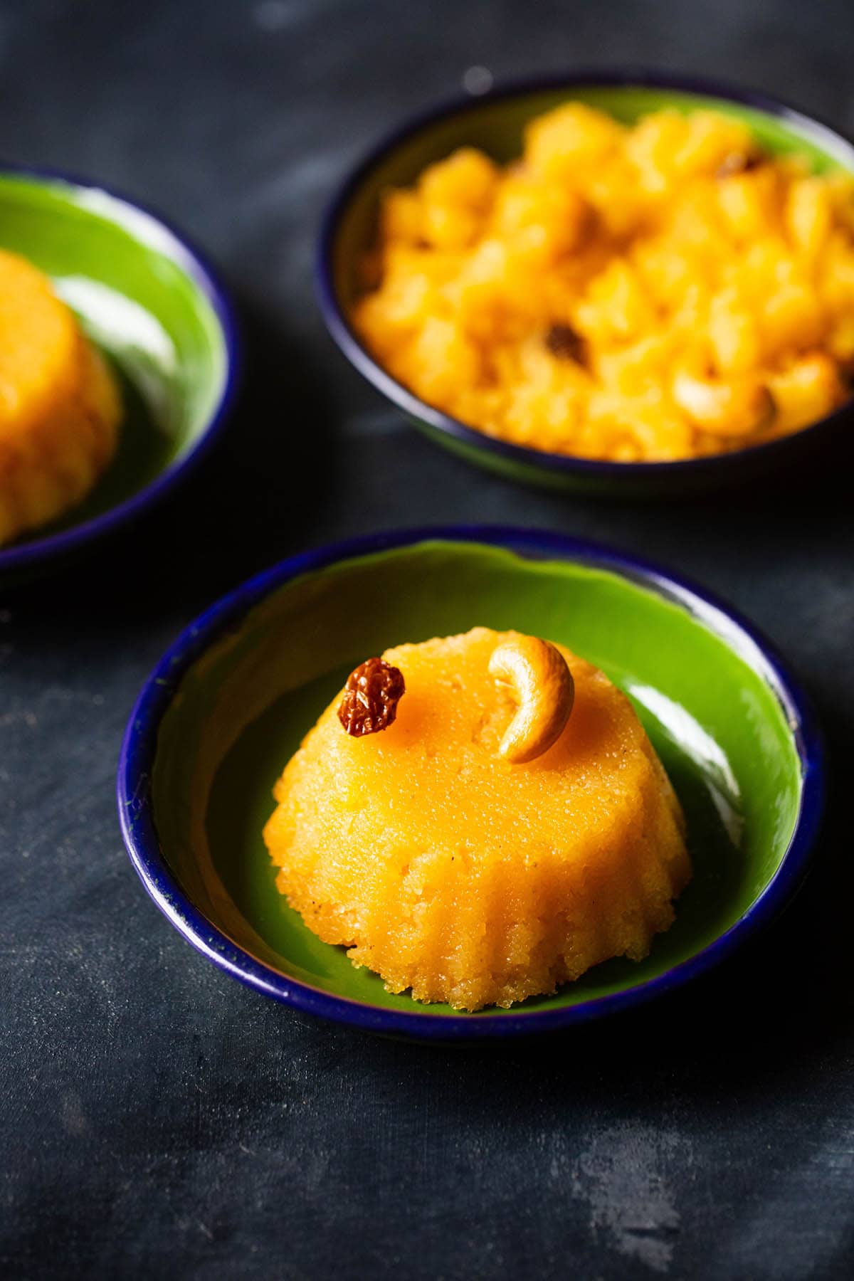 kesari with a cashew and raisin served in a dark green plate on a dark blue-black board