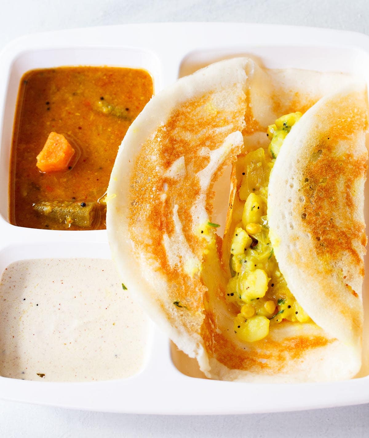 masala dosa opened showing the potato stuffing in a white partitioned tray with sambar and coconut chutney