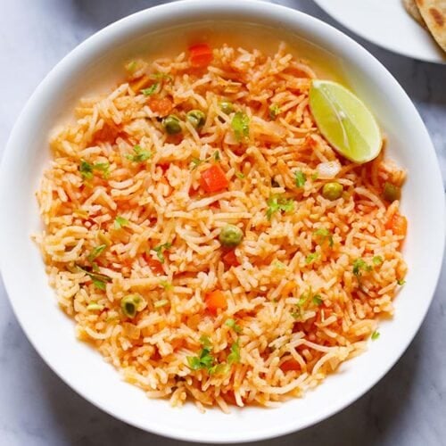 overhead shot of mexican rice with a lemon wedge in a large white bowl