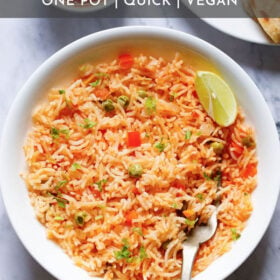 overhead shot of mexican rice with a lemon wedge and a brass fork in the rice in a large white bowl with text layovers