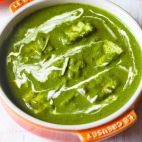 palak paneer topped with cream, garnished with ginger julienne and served in an orange bowl on a white board