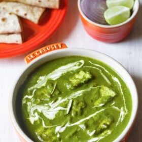 palak paneer topped with cream, garnished with ginger julienne and served in an orange bowl on a white board with text layovers