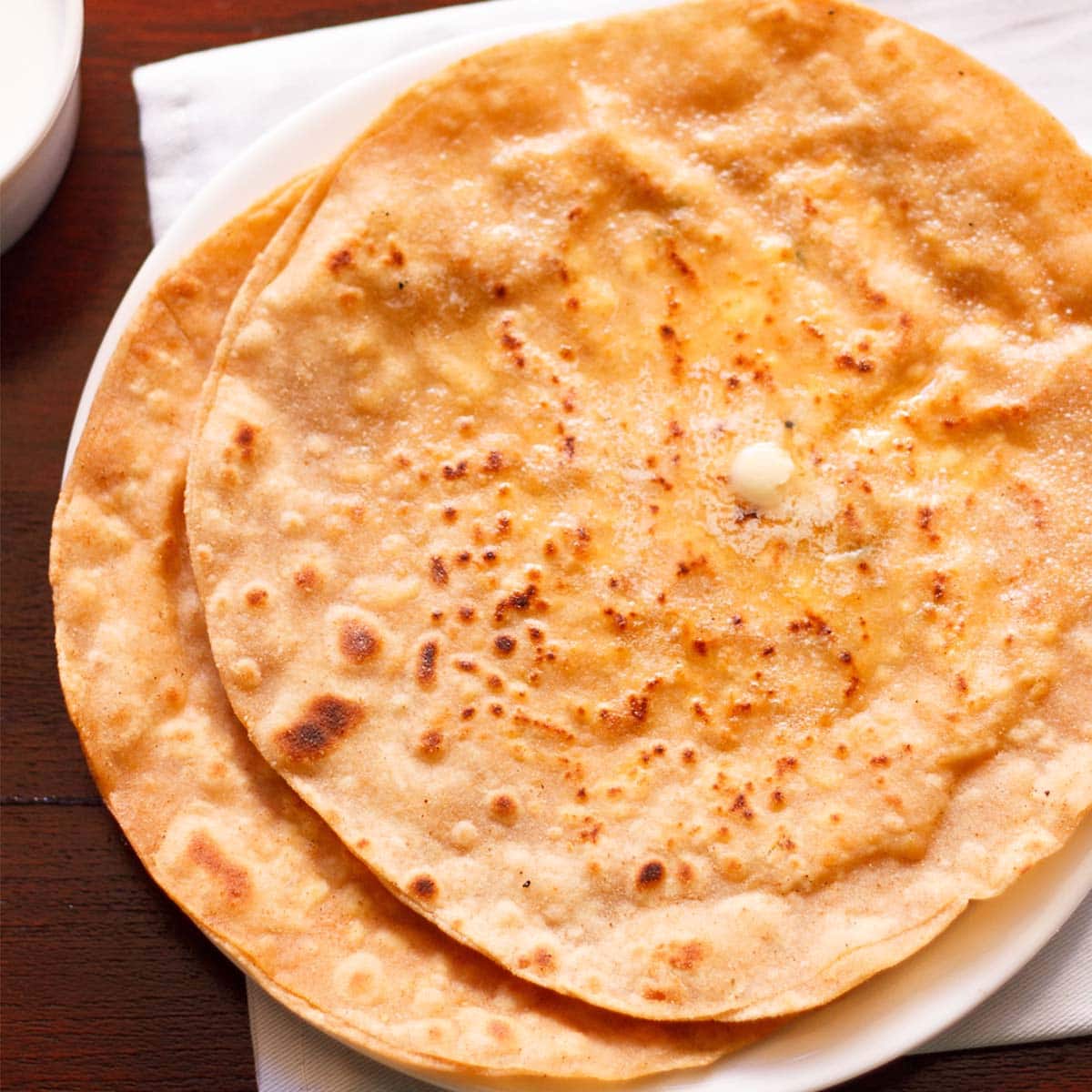 two paneer paratha with butter melting on top on white plate placed on white napkin