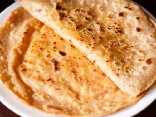 folded paneer paratha on top of a paneer paratha on a white plate.