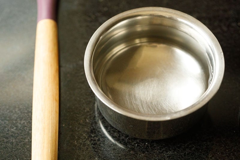 wooden stir stick and metal bowl of water on a black table