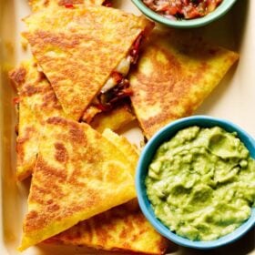 veggie quesadilla triangles served in a tray with a side of guacamole and salsa.