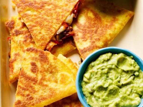 veggie quesadilla triangles served in a tray with a side of guacamole and salsa.