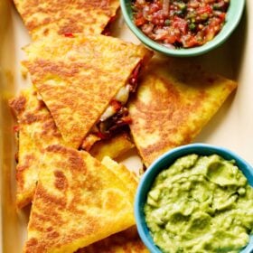 quesadilla triangles served in a tray with a side of guacamole and salsa.