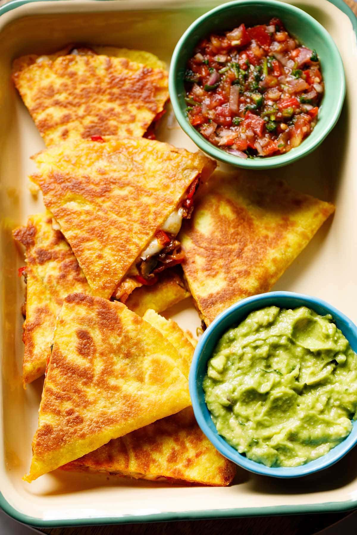 quesadilla triangles served in a tray with a side of guacamole and salsa.