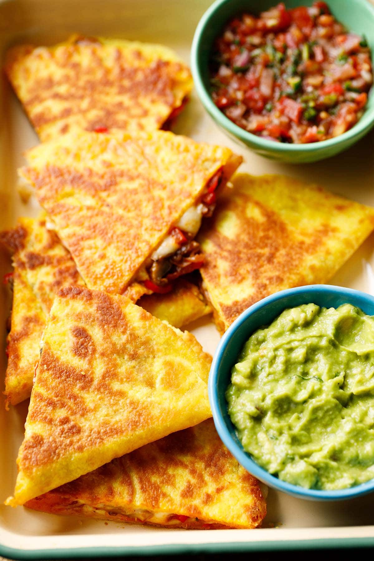 veggie quesadilla triangles served in a tray with a side of guacamole and salsa.