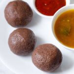 three ragi mudde balls on a white plate with two small bowls of saaru and chilli chutney