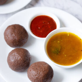 three ragi mudde balls on a white plate with two small bowls of saaru and chilli chutney