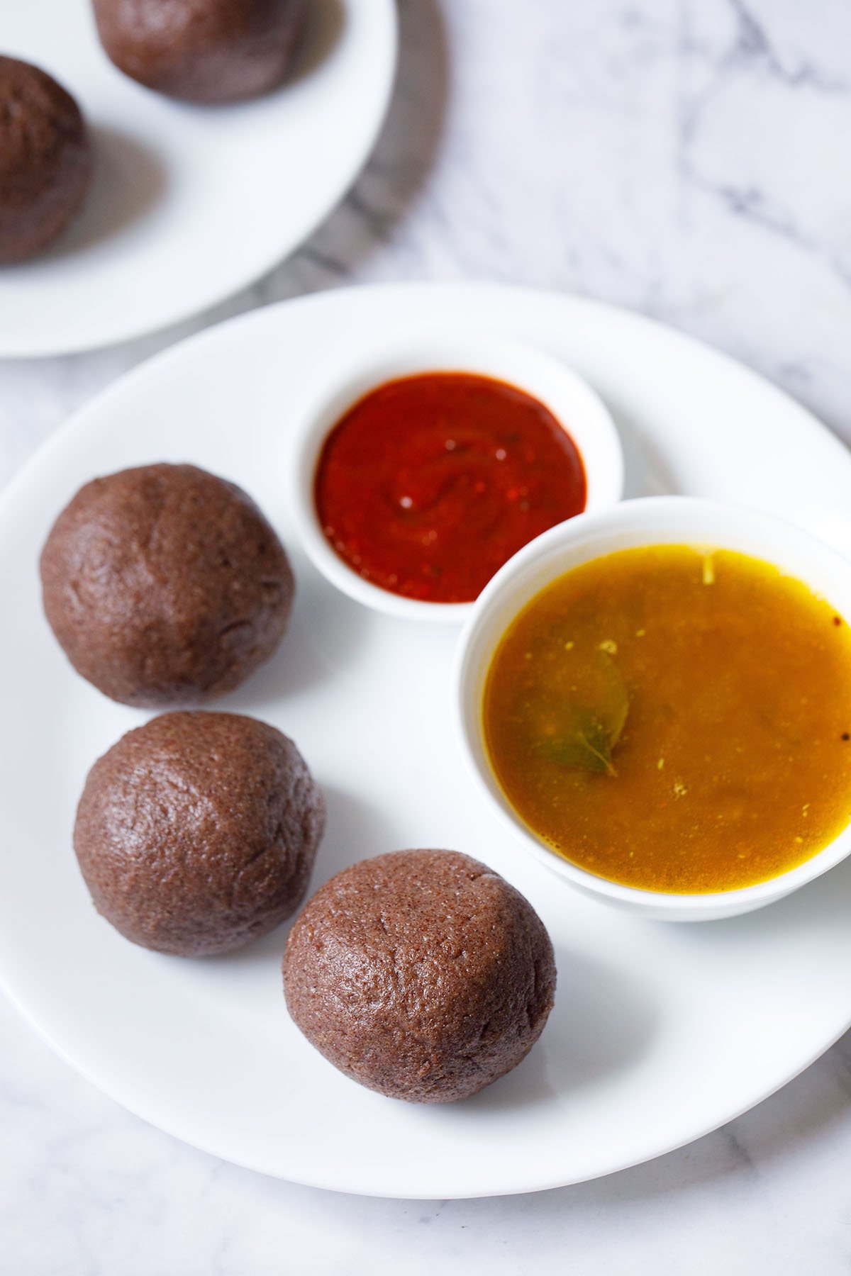 three ragi mudde balls on a white plate with two small bowls of saaru and chilli chutney